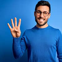 Person with glasses smiling and holding 4 fingers up on their right hand