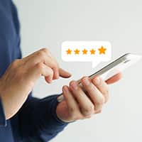 A hand holding a smartphone with a graphic of a five star rating floating above it