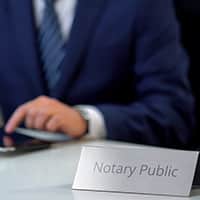 A person in a suit at a desk with a name desk placard that says Notary Public